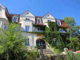 Die Jugendstilvilla &quot;Villa Füglein&quot;, in der sich das Deutsche Fahrradmuseum befindet, wurde im Jahr 1908 erbaut. Auf diesem Bild ist das Haus im Sommer zu sehen, mit grünem wildem Wein bewachsen, Bäumen im Vordergrund uns blauem Himmel im Hintergrund